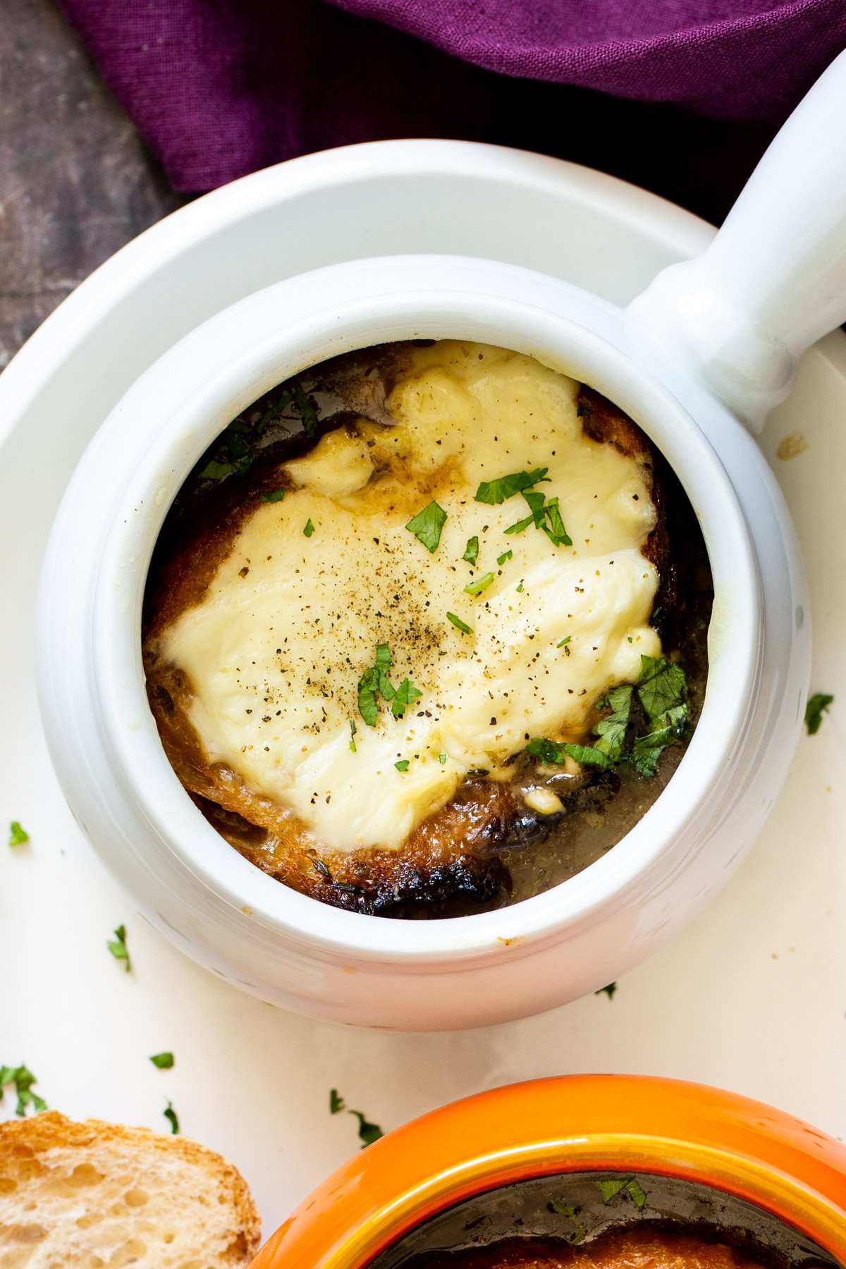 a small white soup bowl with vegan French onion soup topped with a slice of cheese bread