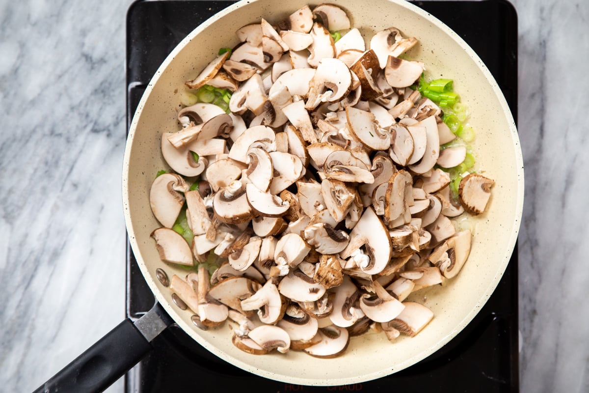 mushrooms and green onions in a sauteeing pan