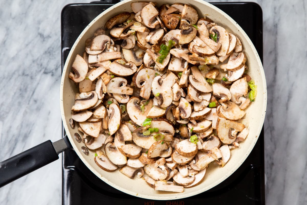 mushrooms and green onions in a sauteeing pan