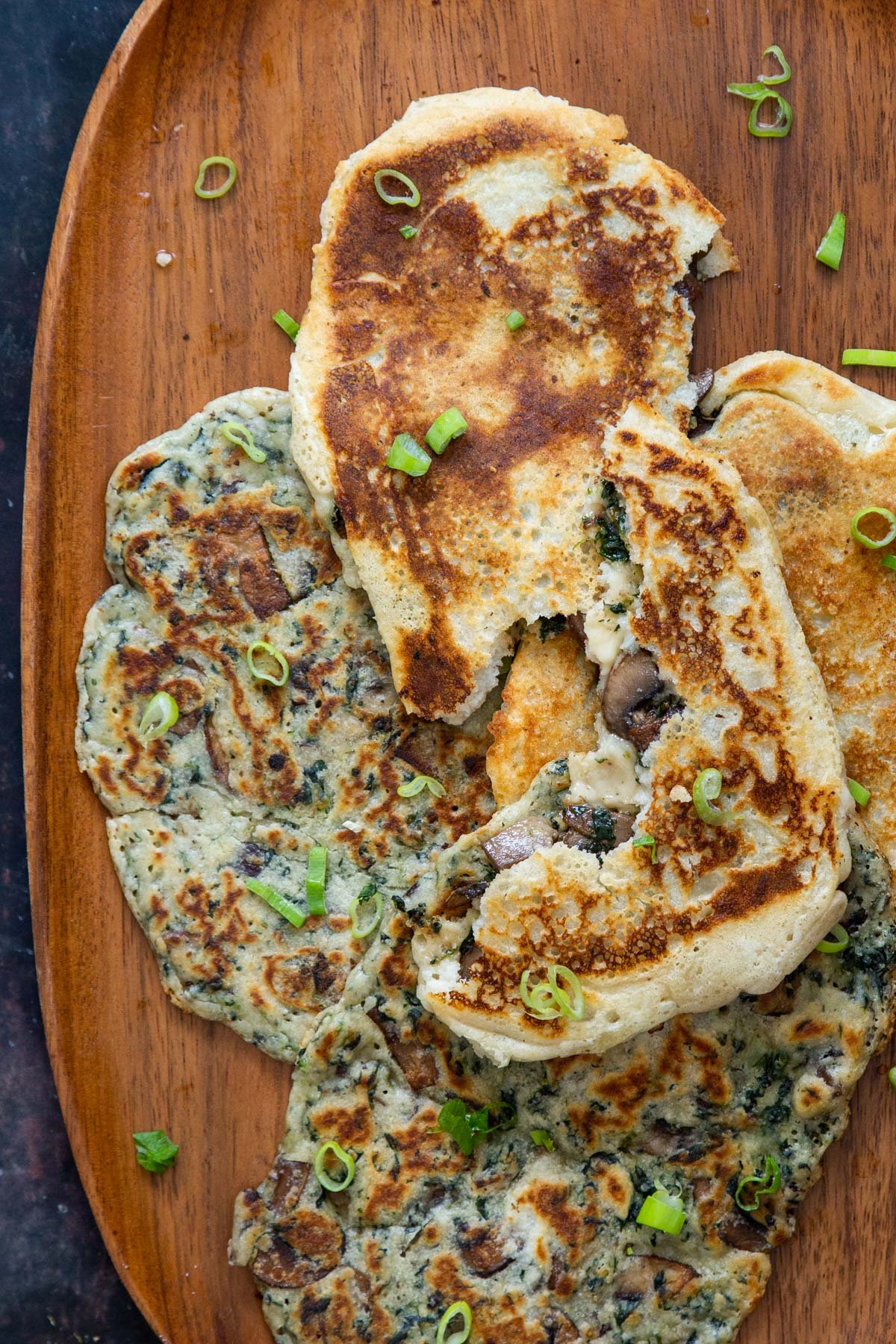 vegan spinach and mushroom stuffed naan bread on a wooden plate sprinkled with sliced green onions