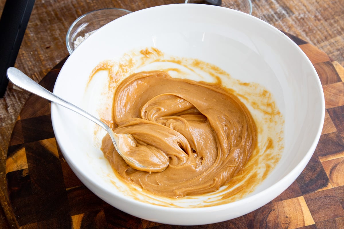 warmed peanut butter in a white bowl being stirred smooth