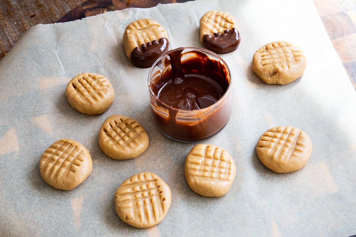 no bake peanut butter cookies with a small bowl of melted chocolate on a sheet of parchment paper