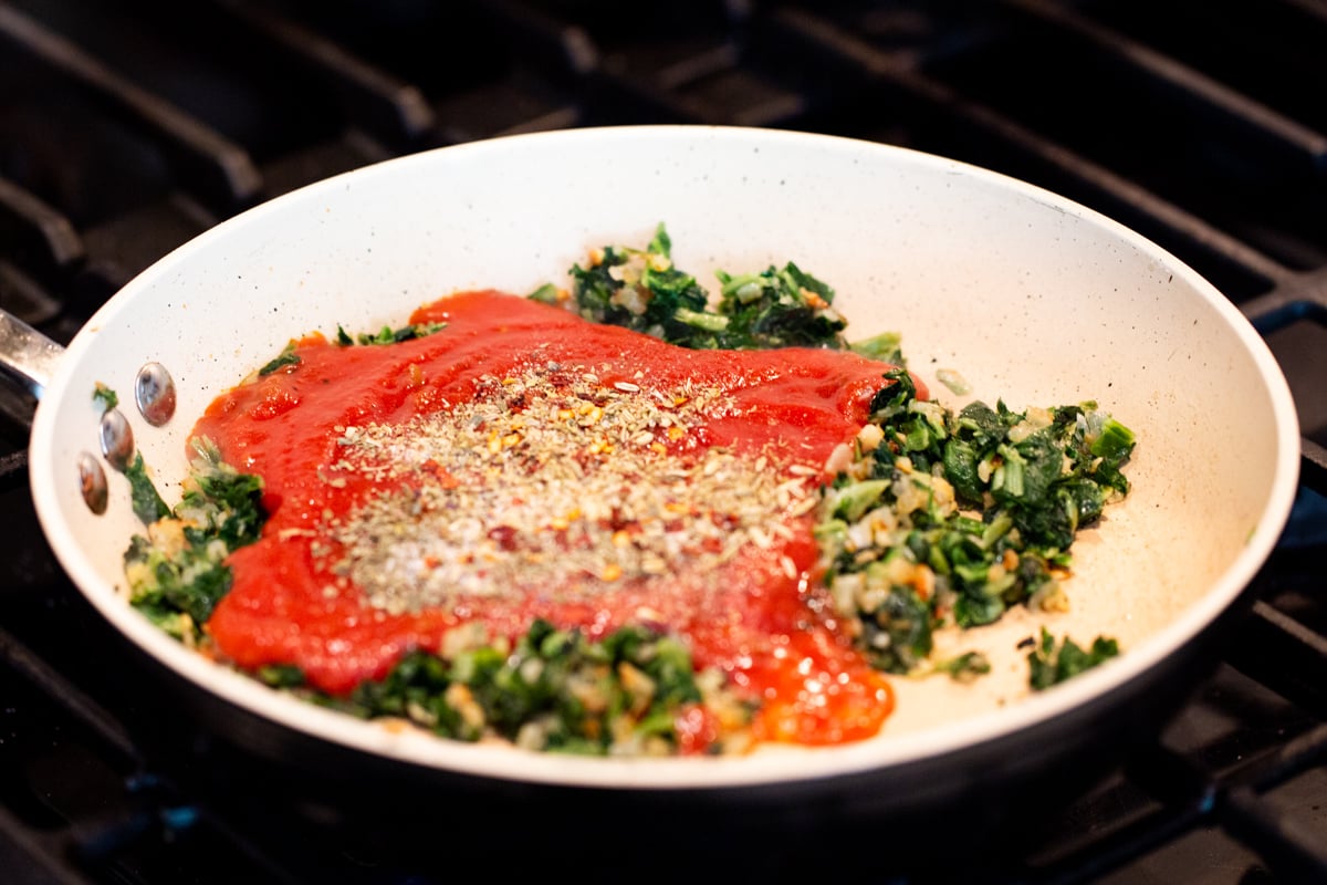 minced onions and spinach with tomato puree in a small sauteeing pan