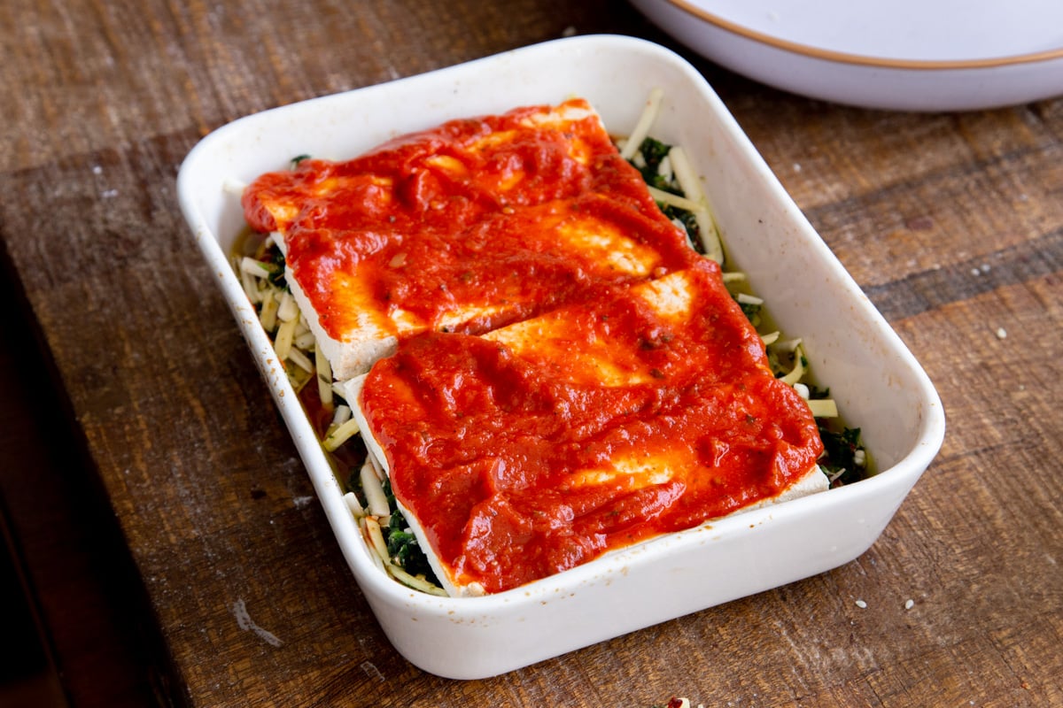 tofu parmesan bake being layered in a casserole dish