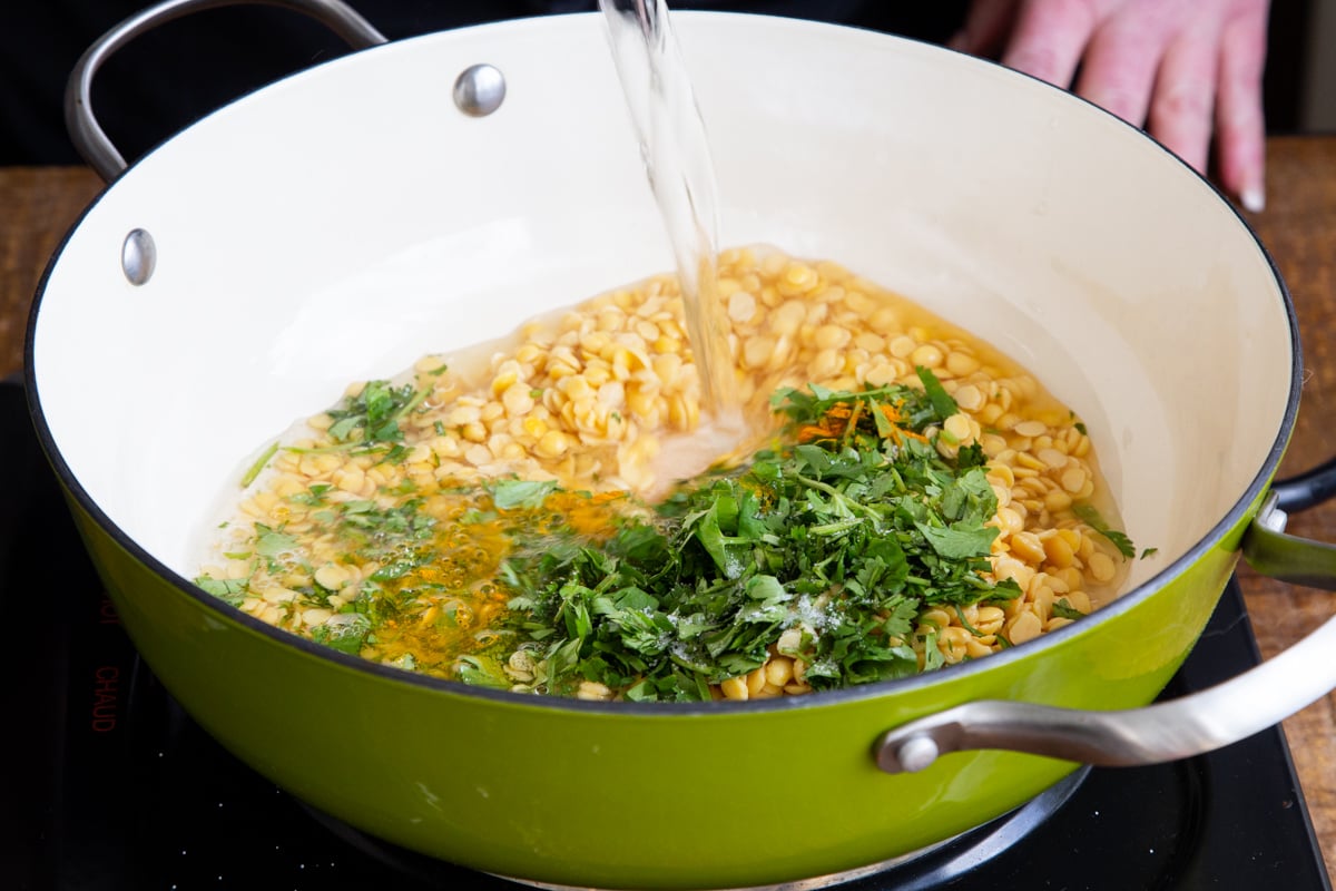 water being poured into a sauteeing pan with lentils and cilantro