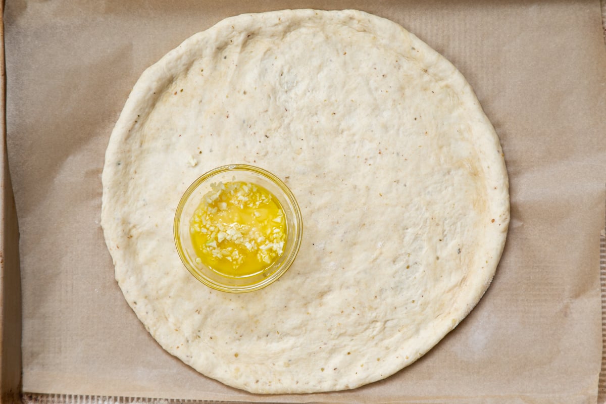 vegan pizza dough shaped into a circle on a baking sheet with a small dish of garlic oil on the crust