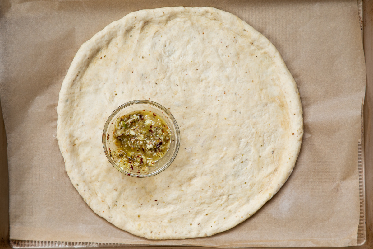 shaped pizza dough on a baking sheet with a small dish of seasoned oil