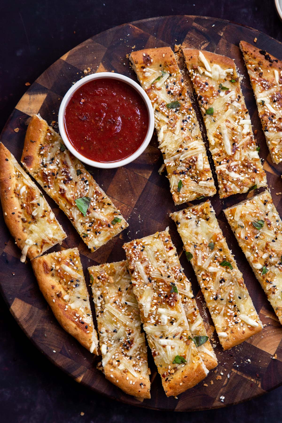 vegan cheese breads sticks on a wooden board with a small dish of marinara sauce