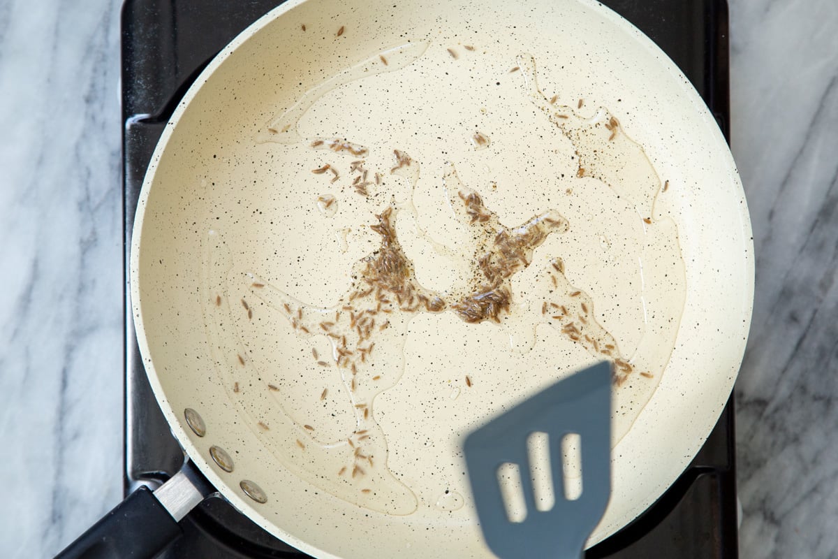 whole cumin seeds being tempered in a pan in hot oil