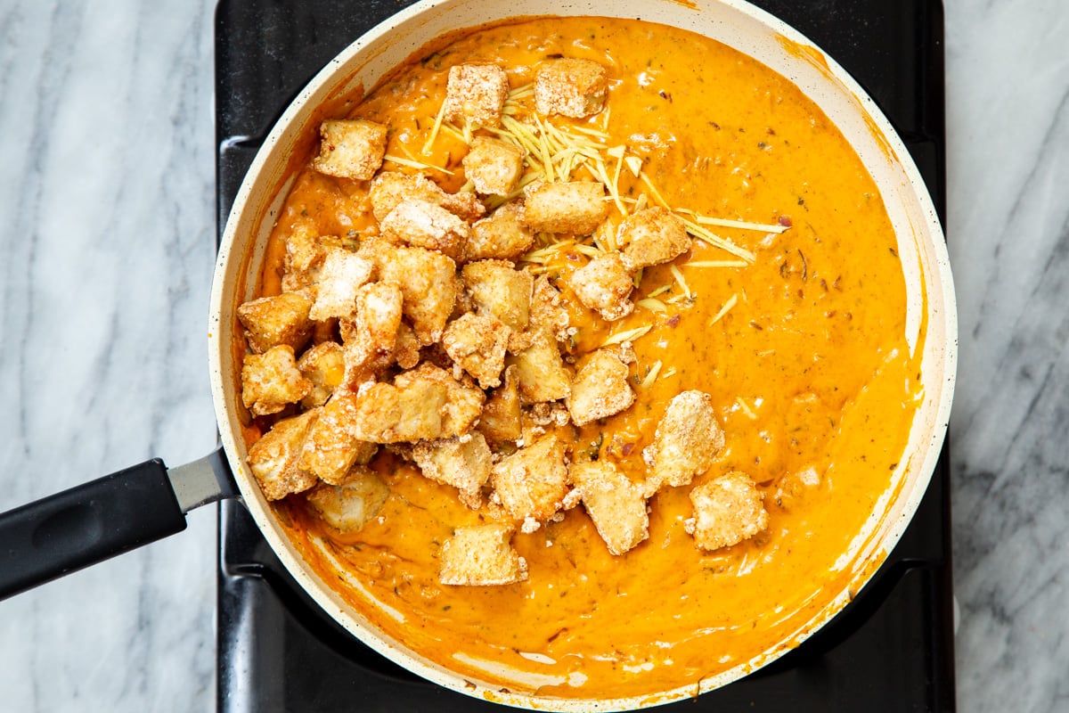 baked tofu chunks being added to pan with creamy red bell pepper sauce