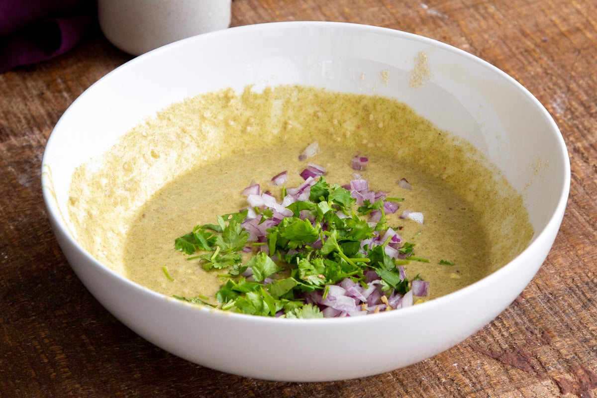 vegan lentil pancakes batter in a white bowl topped with chopped onions and cilantro