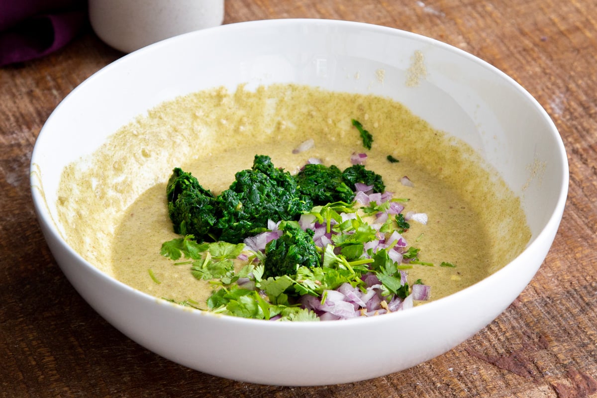 vegan lentil pancake batter in a white bowl with spinach, onion and cilantro