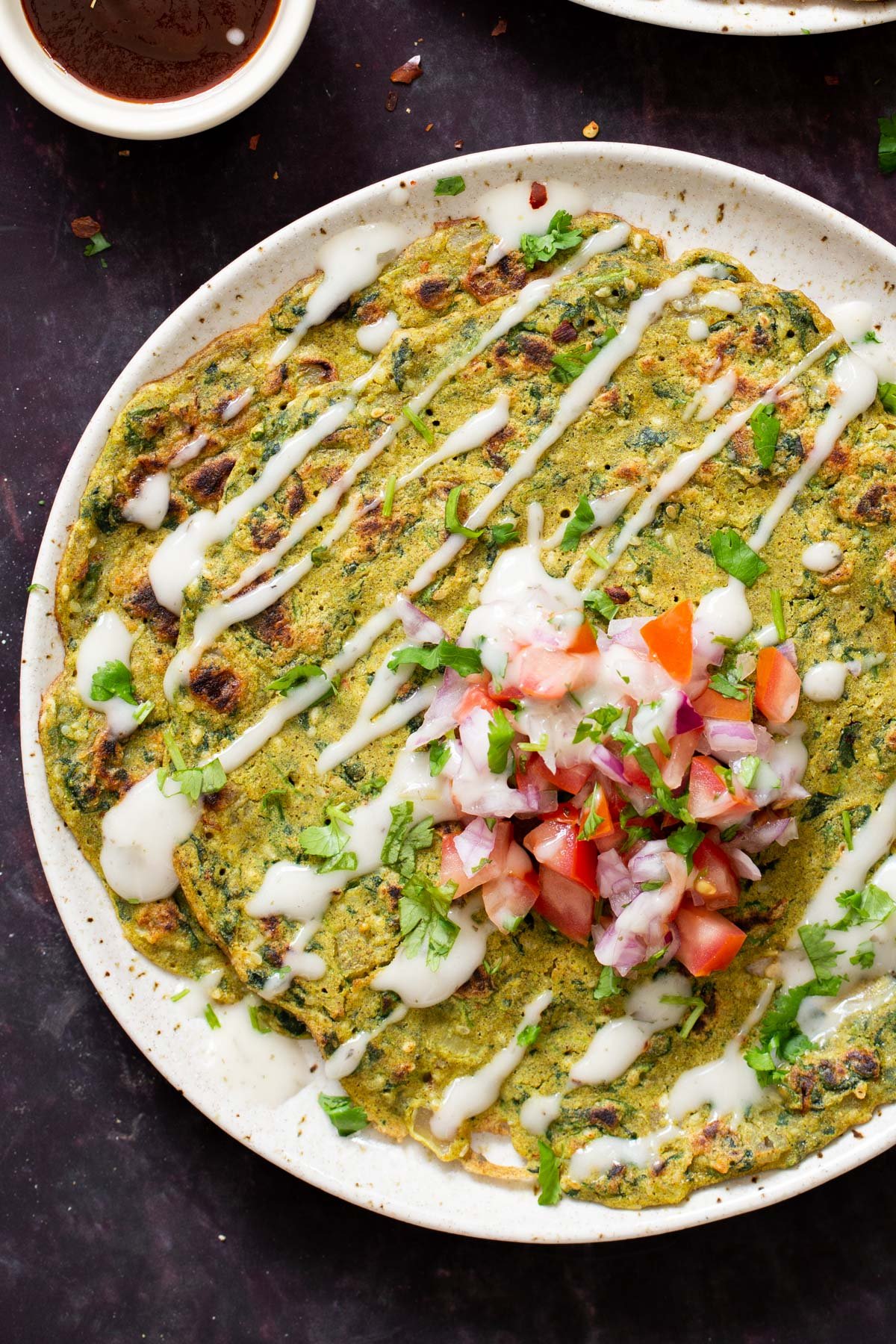 a plate with vegan pancakes drizzled with vegan sour cream and topped with tomatoes and onions
