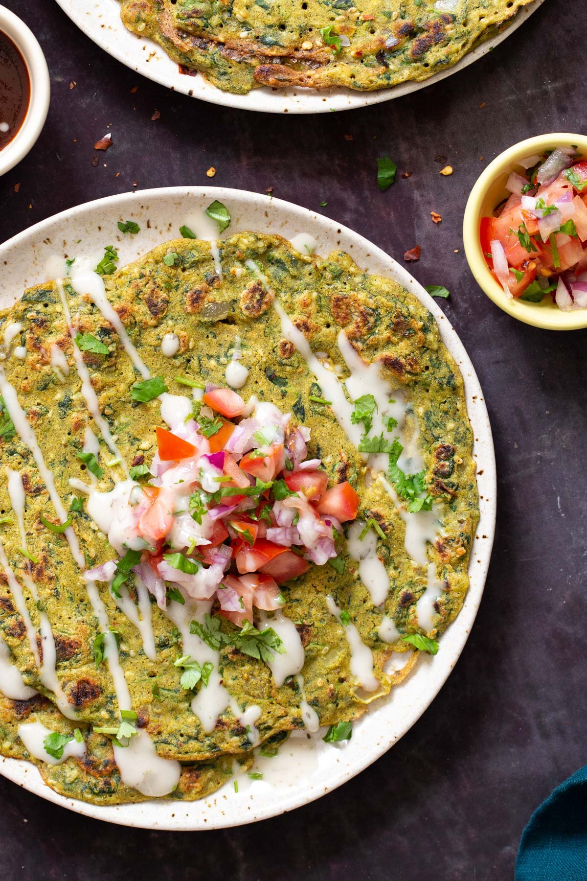a plate with vegan lentil pancakes topped with onion tomato salad, drizzled with sour cream and sprinkled with cilantro