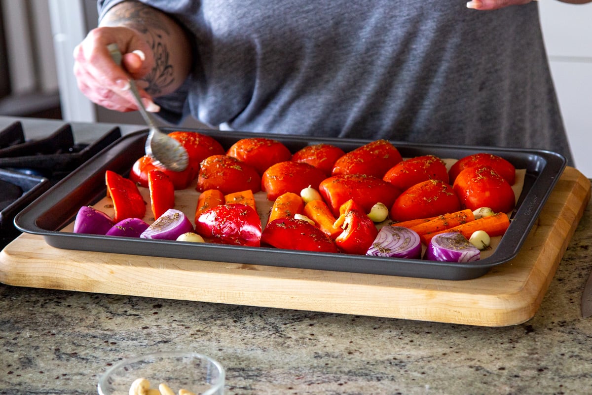 bell pepper, tomatoes and onion on a baking sheet being drizzled with seasoned oil