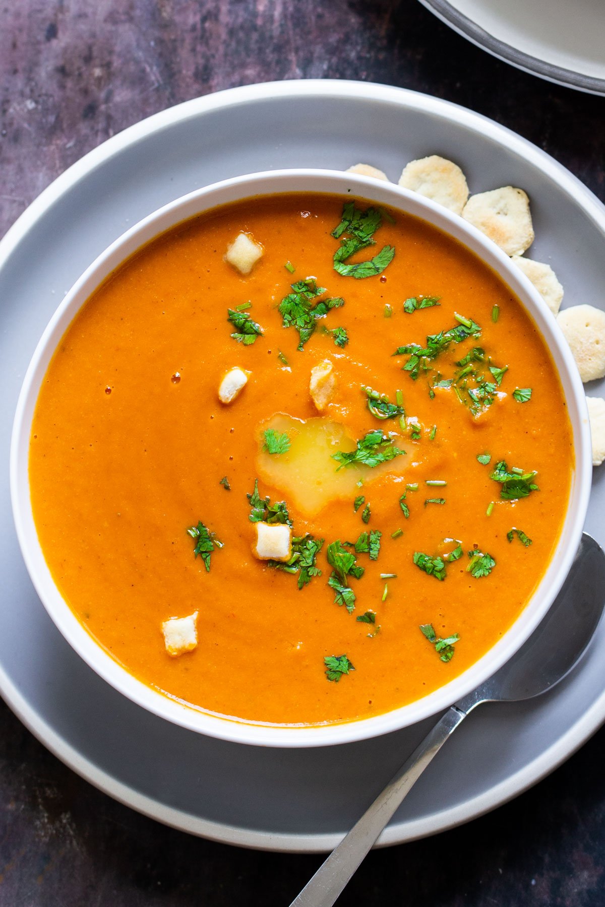 a plate of vegan oven roasted tomato soup on a pale blue plate with crackers on the side