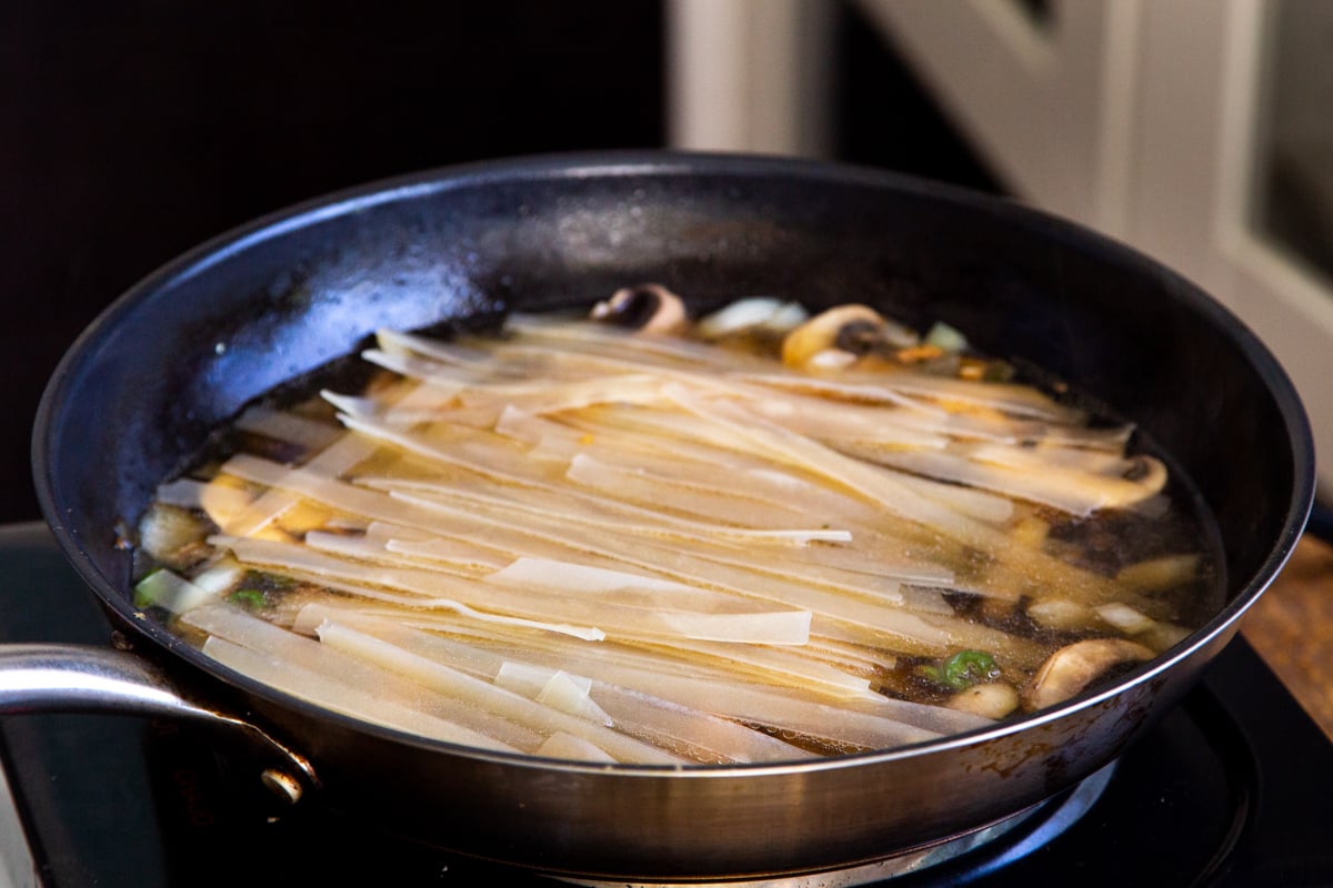 water being added to skillet with rice noodles and veggies for one pan skillet noodle recipe