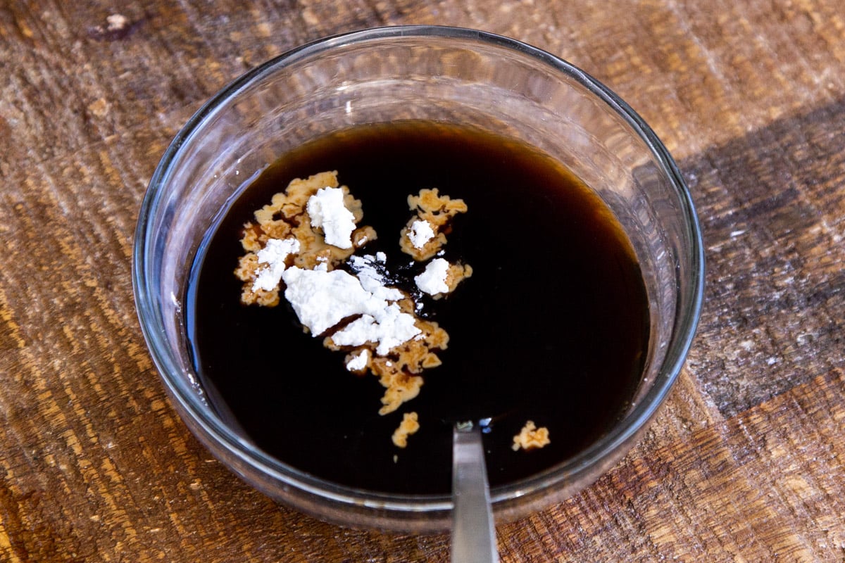 cornstarch being added to a small glass dish with soy sauce to make stirfry sauce