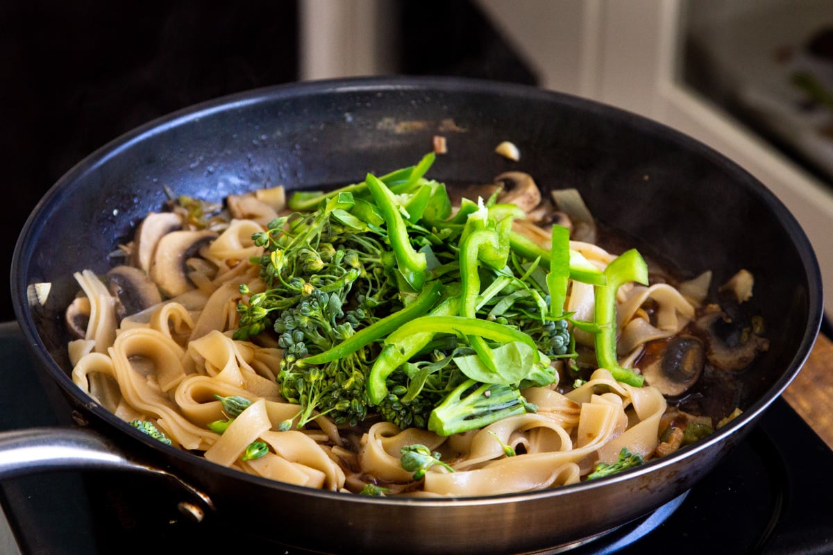 broccoli being added to skillet with noodles