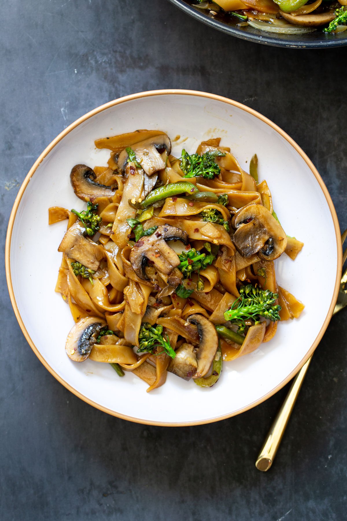 Thai Skillet Noodles with vegetables on a white plate with a golden fork on the side