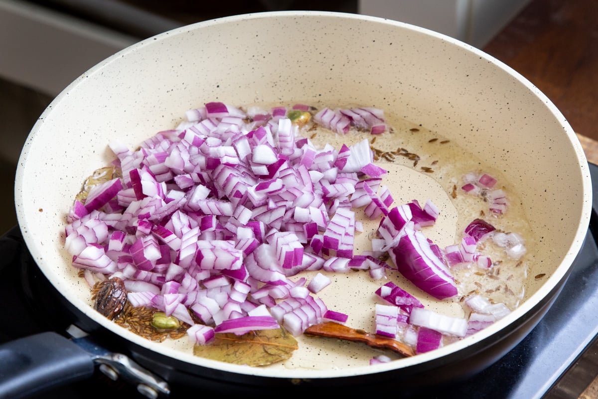 a sauteeing pan with chopped onions and whole spices