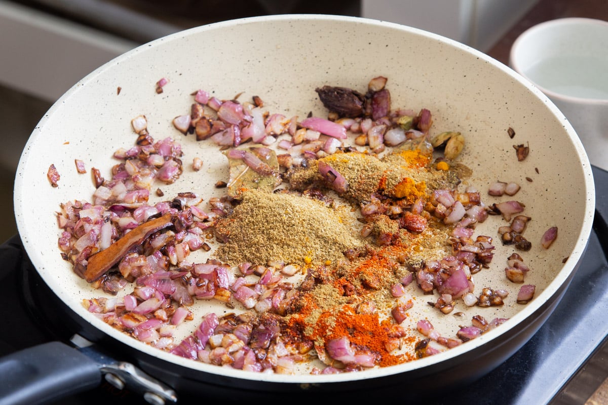 ground spices being added to a sauteeing pan with chopped onions