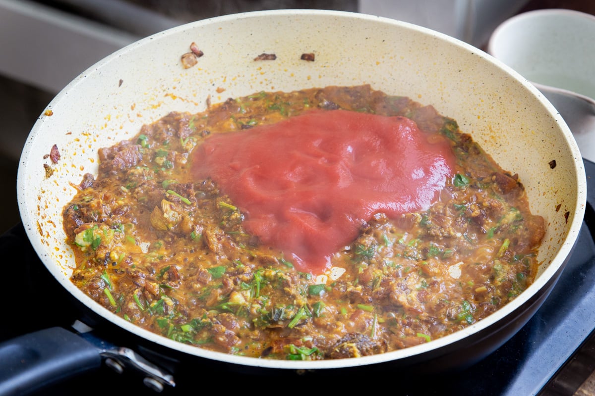a sauteeing pan with chopped onion, tomato puree and cilantro