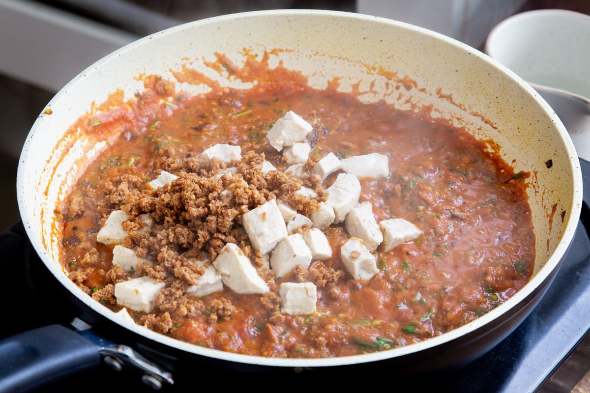 vegan crumbles and tofu being added to a pan with vegan chicken balti