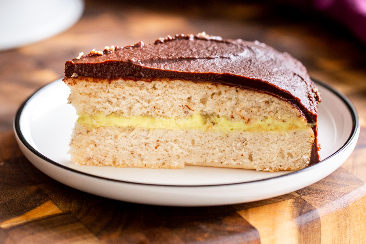 a slice of vegan boston cream pie cake on a wooden board