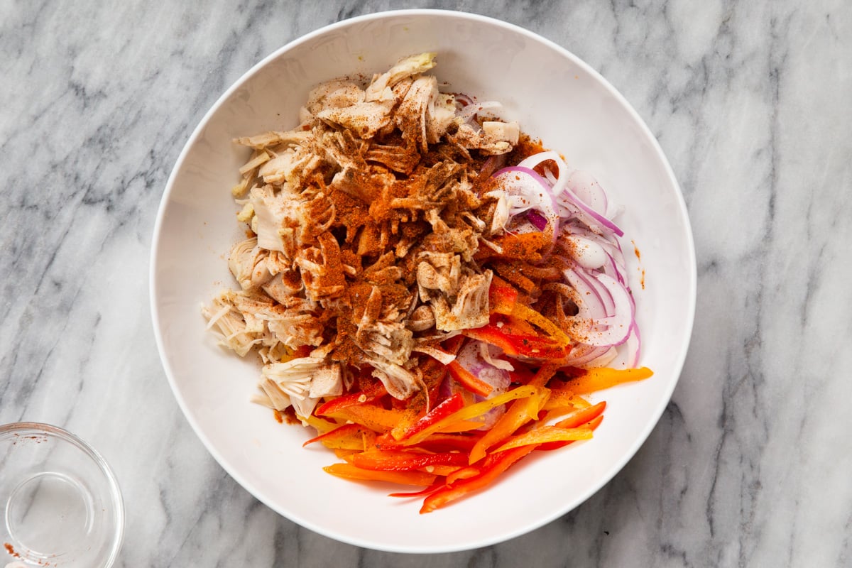 shredded jackfruit in a white bowl with spices, bell pepper and onions