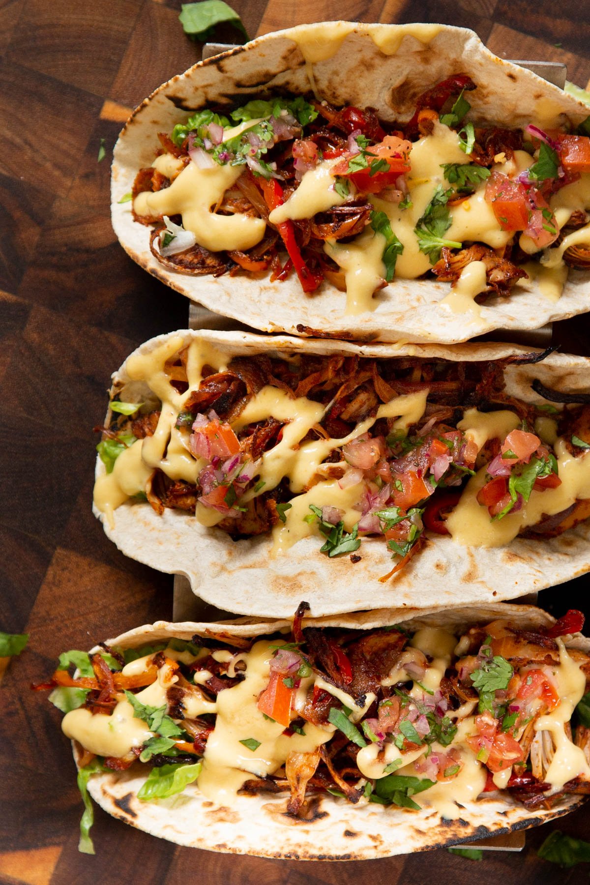 three jackfruit tacos topped with vegetables and cheese sauce