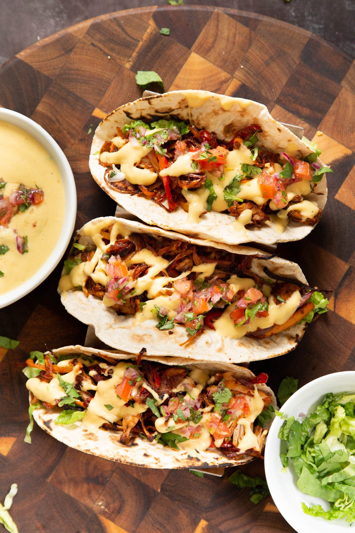 three vegan Jackfruit tacos topped with veggies and cheese sauce