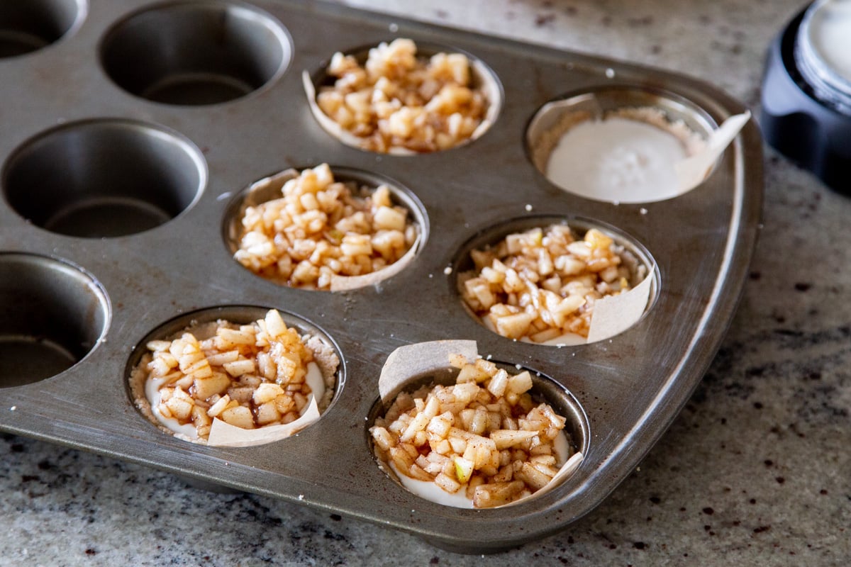 mini vegan apple cheesecakes in a muffin tin ready for baking