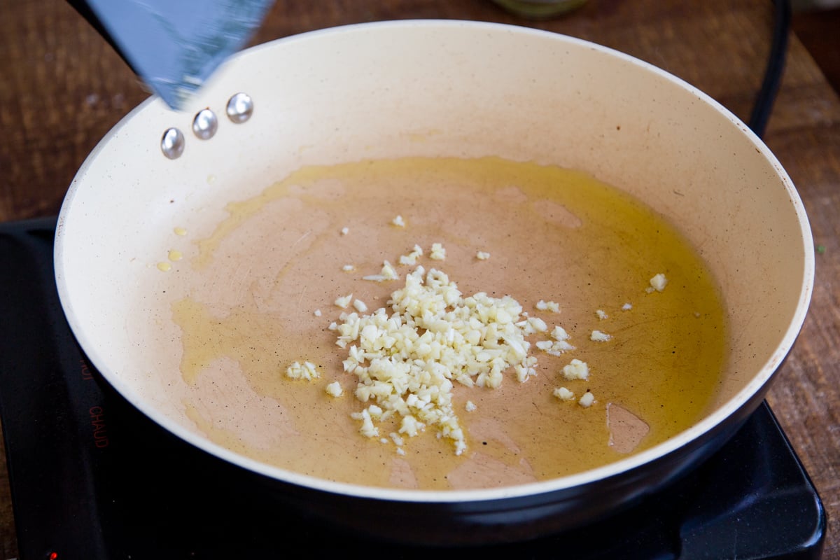 adding garlic to a pan of oil
