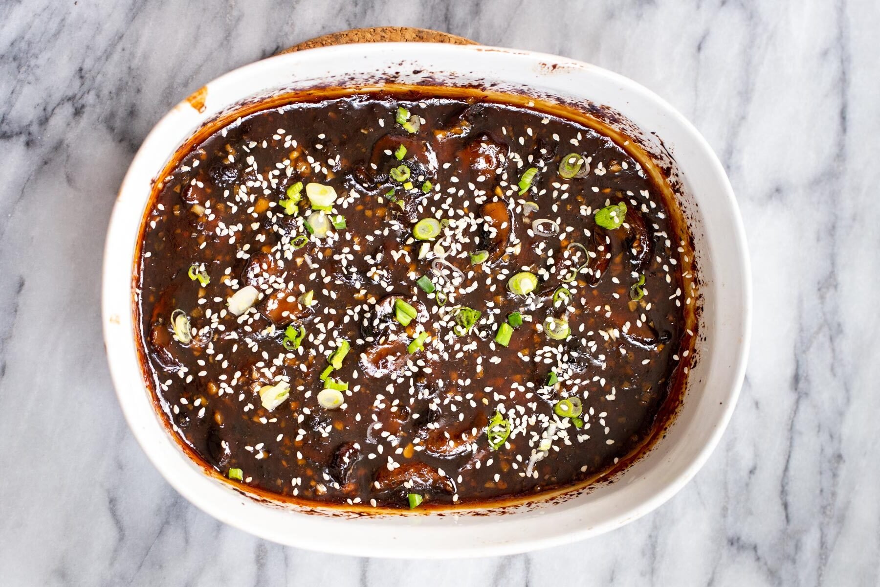 sticky sesame mushrooms in a casserole dish sprinkled with sesame seeds and green onions