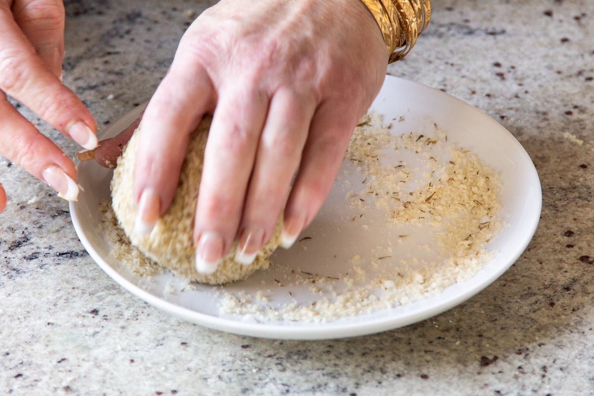 vegan cheese balls being rolled on a plate with coating 