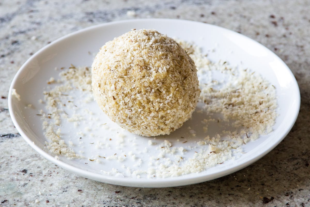 vegan cheese ball being coated breadcrumbs and seasonings
