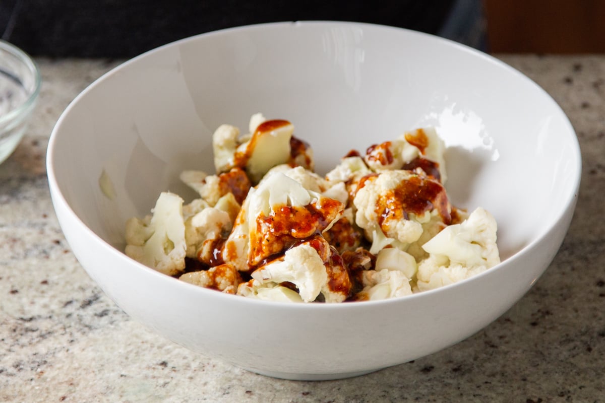 cauliflower florets in a small bowl being drizzled with spicy sauce