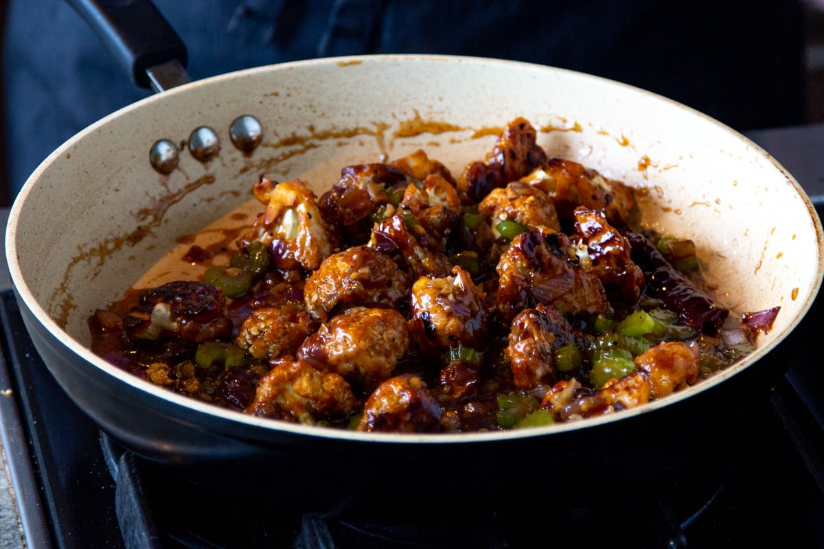 baked cauliflower being tossed with sweet and spicy sauce in a sauteeing pan