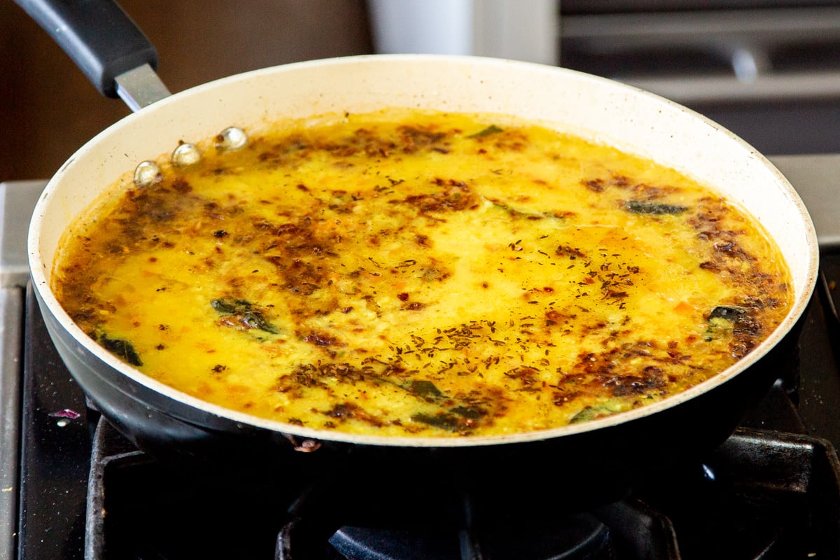 tempered oil being poured over a pan with yellow lentil dal