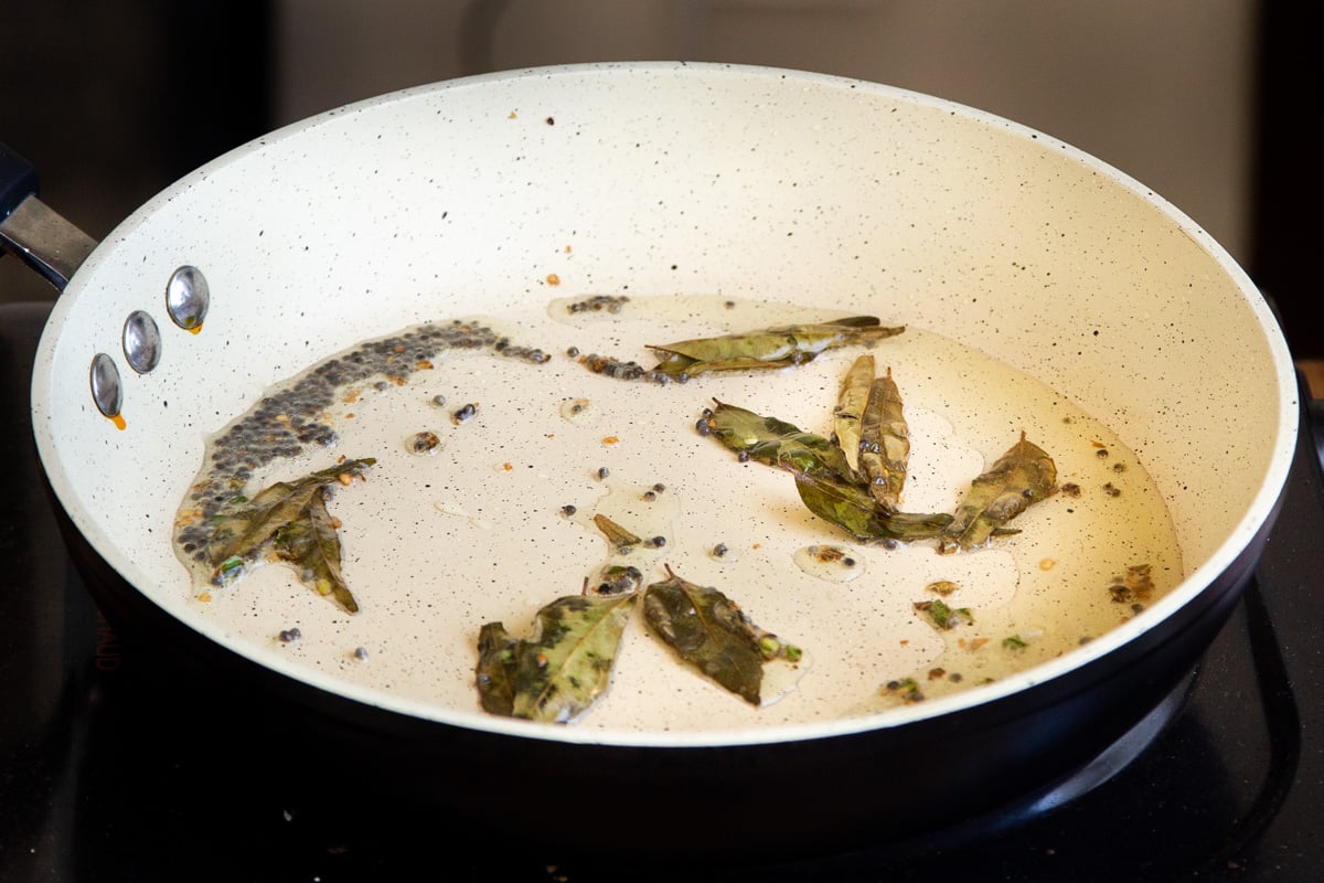 curry leaces and mustard seeds frying in a pan