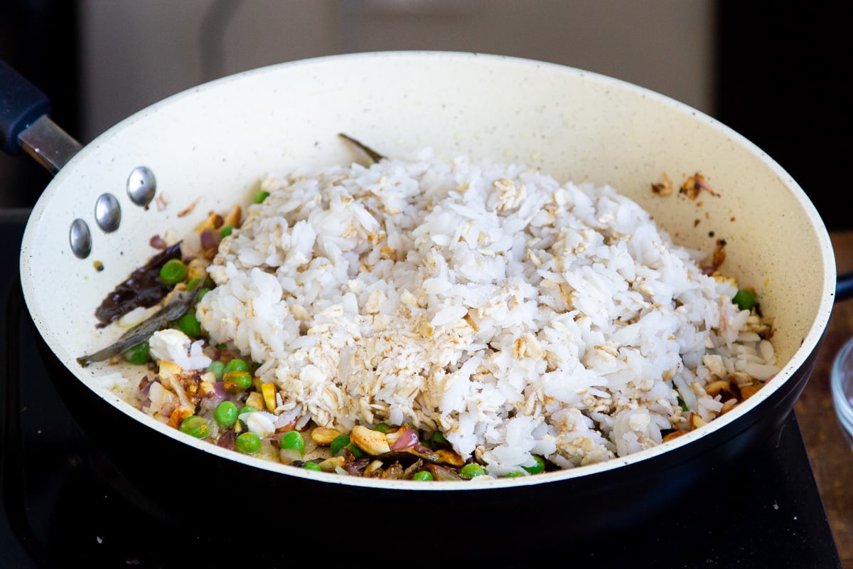 poha flakes and oats being added to a pan with peas and spices