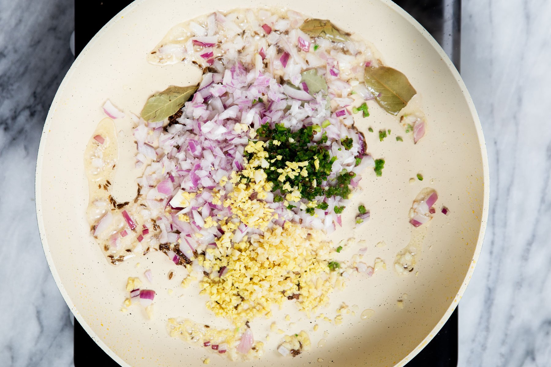 minced ginger and diced onion in a sauteeing pan with spices 
