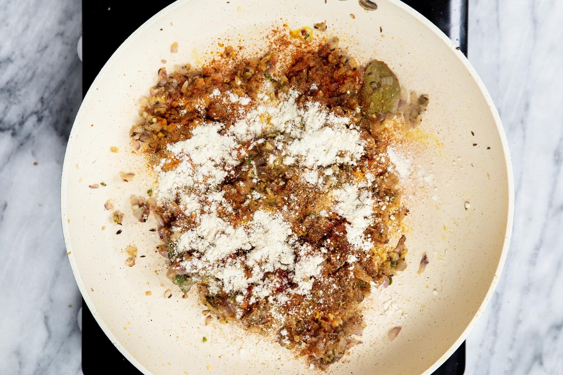 flour being added to a sauteeing pan with ginger and onion 