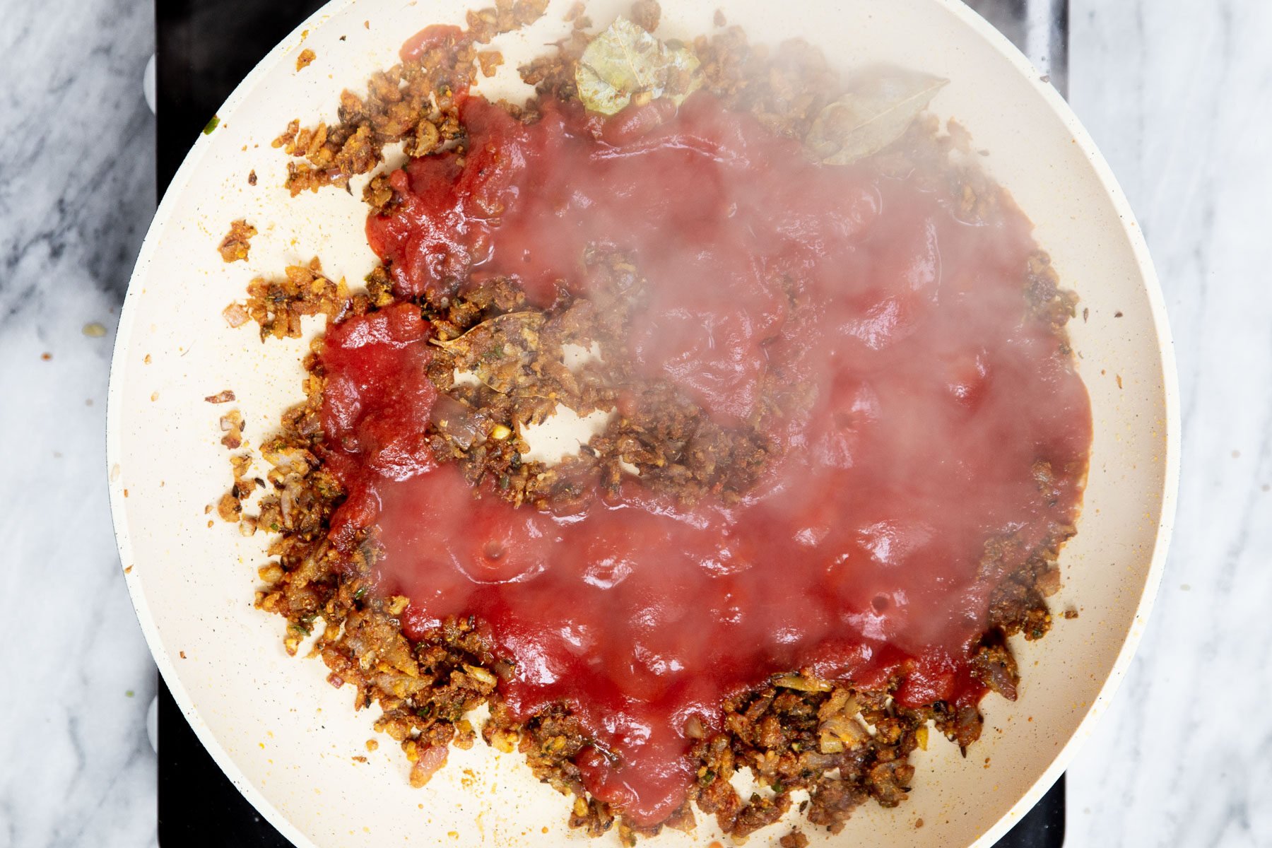 tomato paste being added to a sauteein pan with onion and spices 