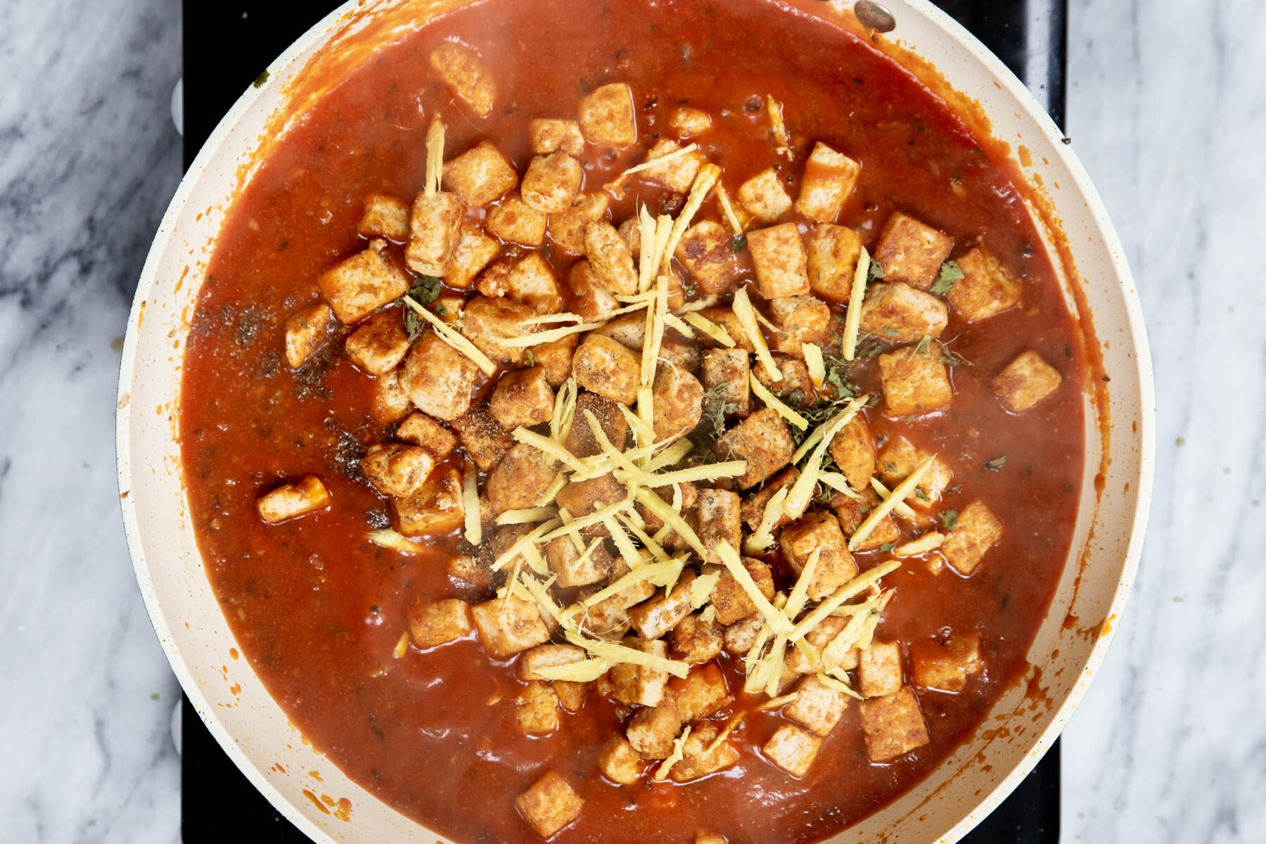 baked tofu being added to a sauteeing pan with spiced tomato sauce 