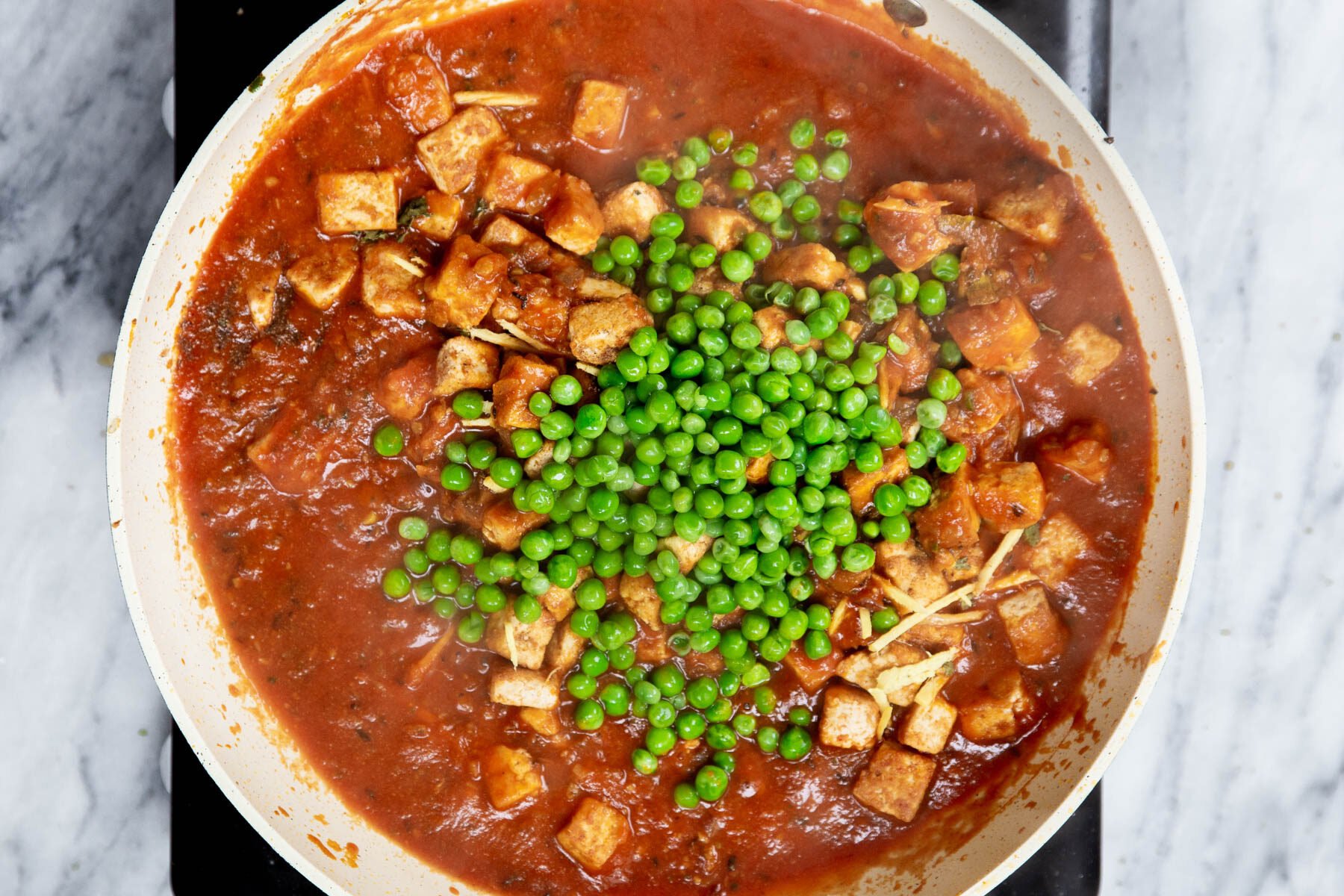 peas being added to Indian tofu curry in a sauteeing pan