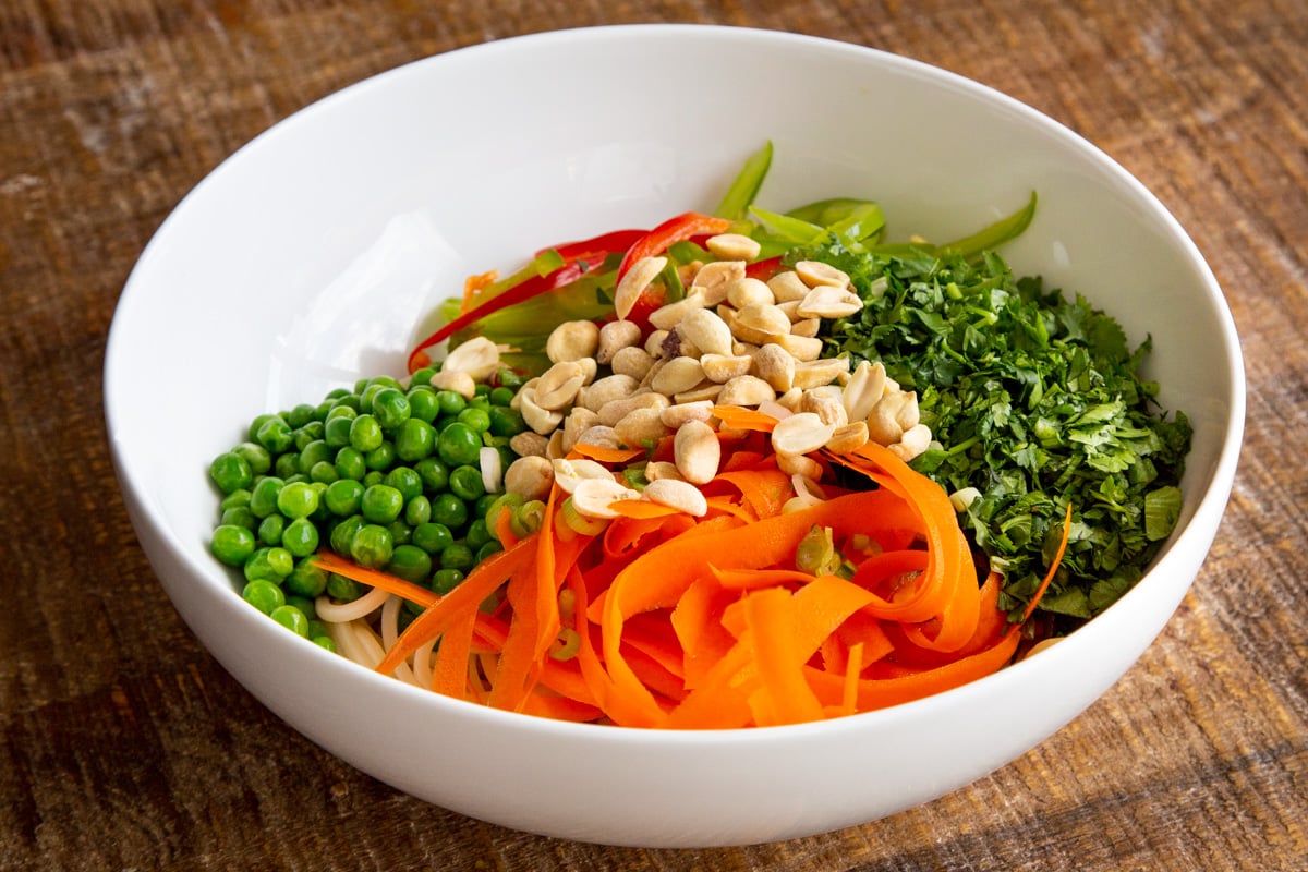 veggies and cooked spaghetti in a white bowl sprinkled with peanuts
