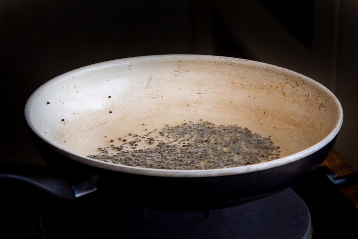 mustard seeds being tempered in a pan with oil