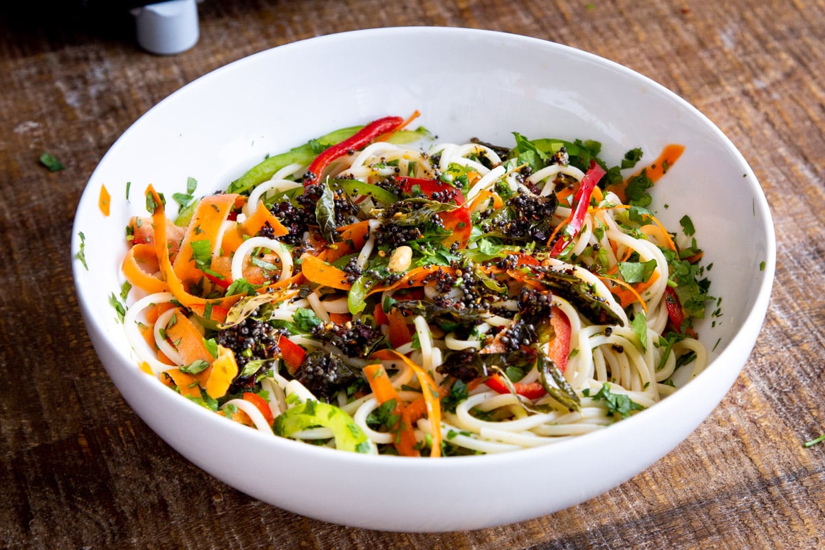 pasta salad, and veggies with tadka tempering being mixed in a white salad bowl